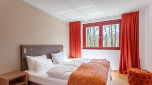 Une chambre moderne avec un grand lit, une table de chevet, une fenêtre avec des rideaux et une vue sur les arbres.