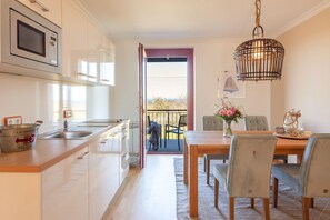 Une cuisine moderne dotée d’un four à micro-ondes encastré, un coin repas avec une table et des chaises en bois, et une vue sur l’extérieur grâce à une porte ouverte.