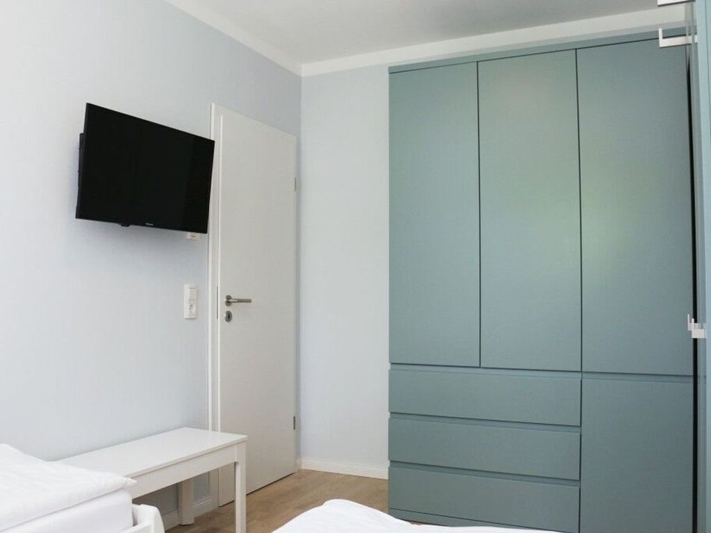 Ein Schlafzimmer mit einem Bett, einem weißen Schreibtisch, einem an der Wand montierten Fernseher und einem großen Kleiderschrank.