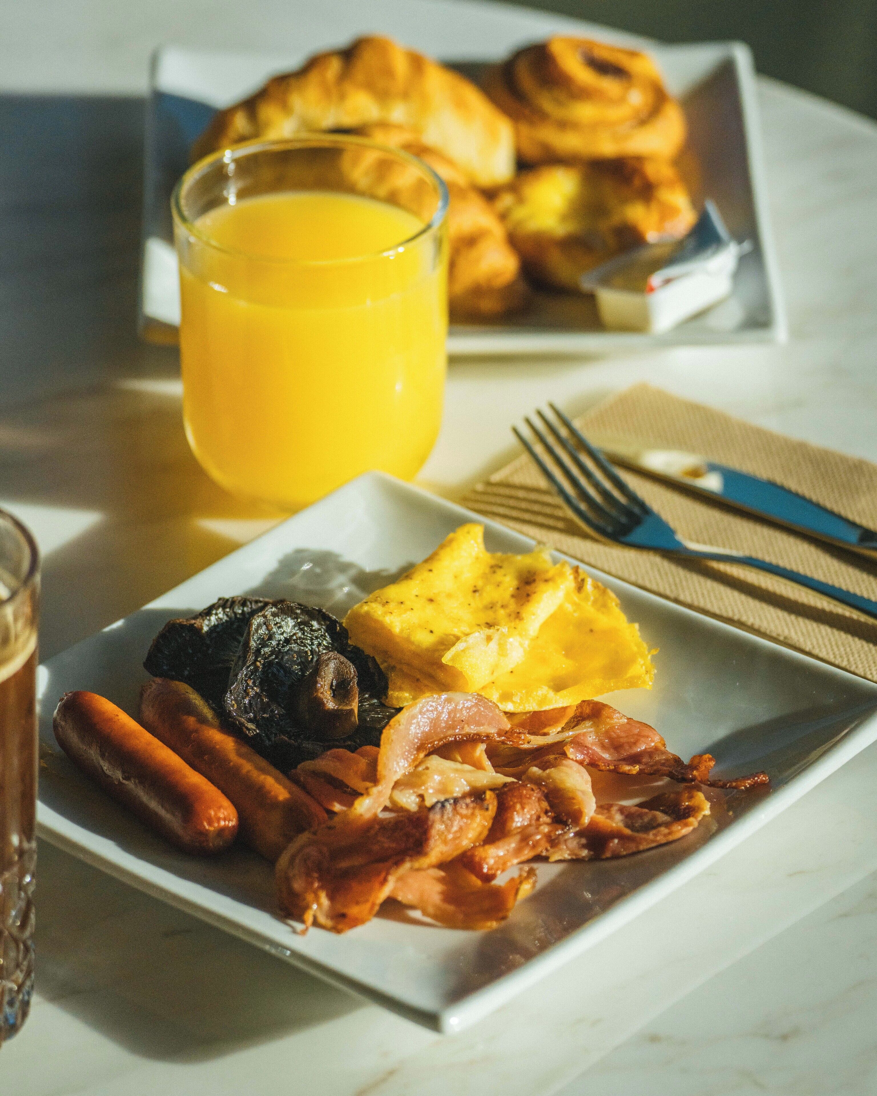 A breakfast plate with eggs, bacon, sausages, and a glass of orange juice.