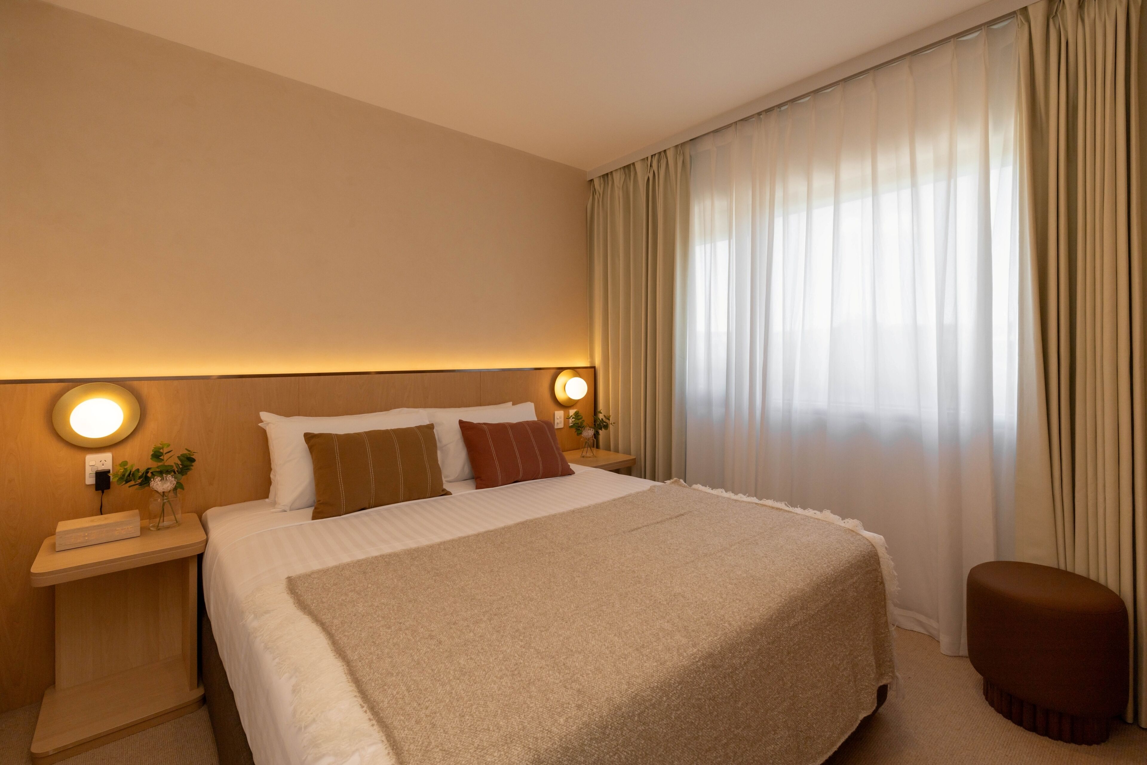 A hotel room with a large bed, a bedside table with a lamp, and a window with curtains.