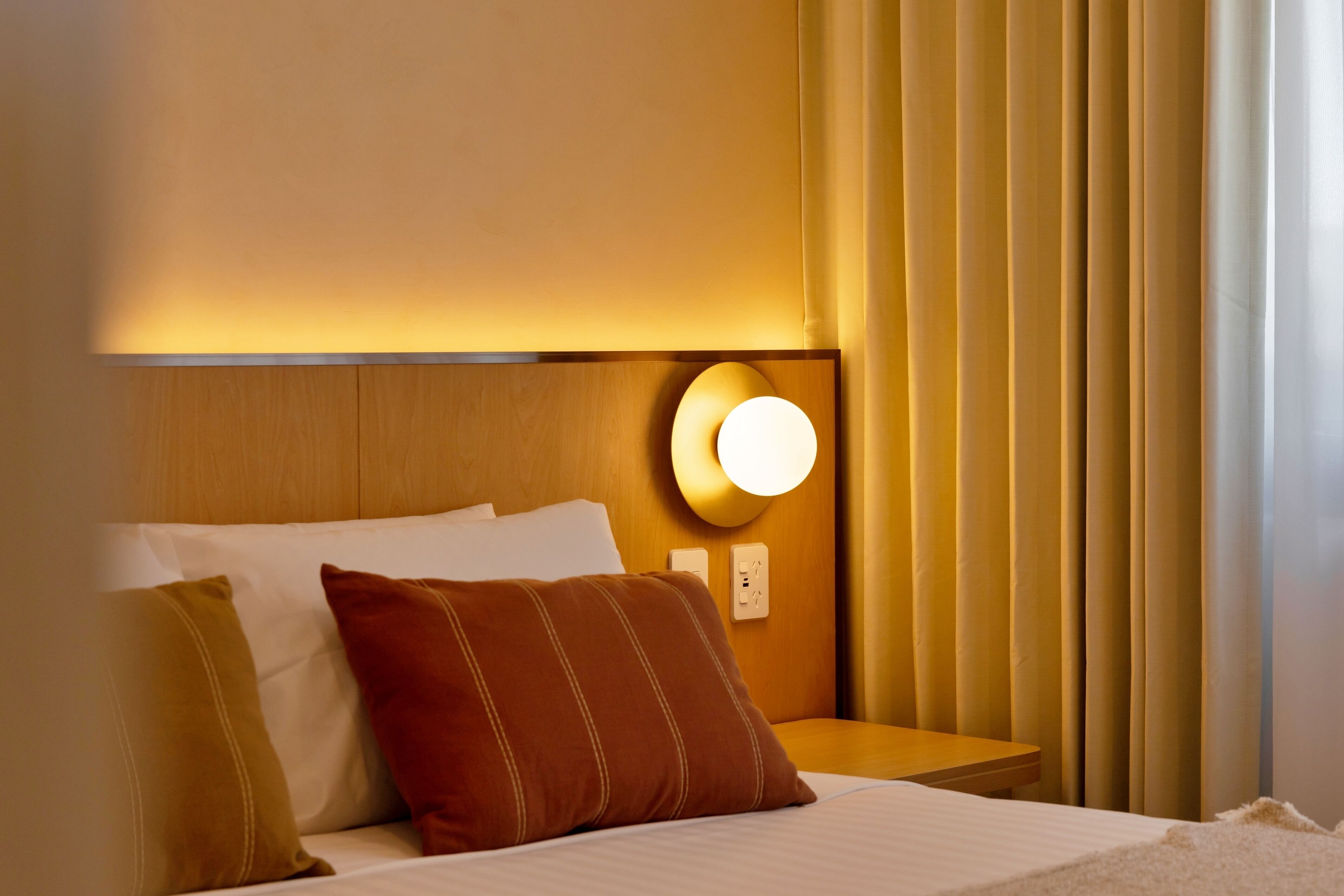 Ein Hotelzimmer mit Bett, Kissen, einem Nachttisch, einer Wandleuchte und Vorhängen.