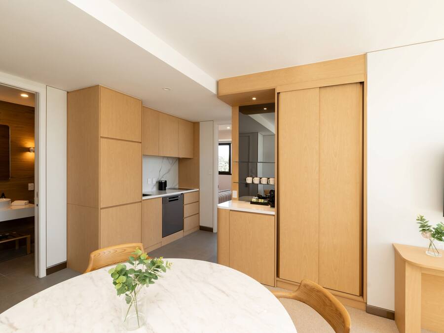 A modern kitchen with wooden cabinets, a dining area with a marble table, and a small plant on the side table.