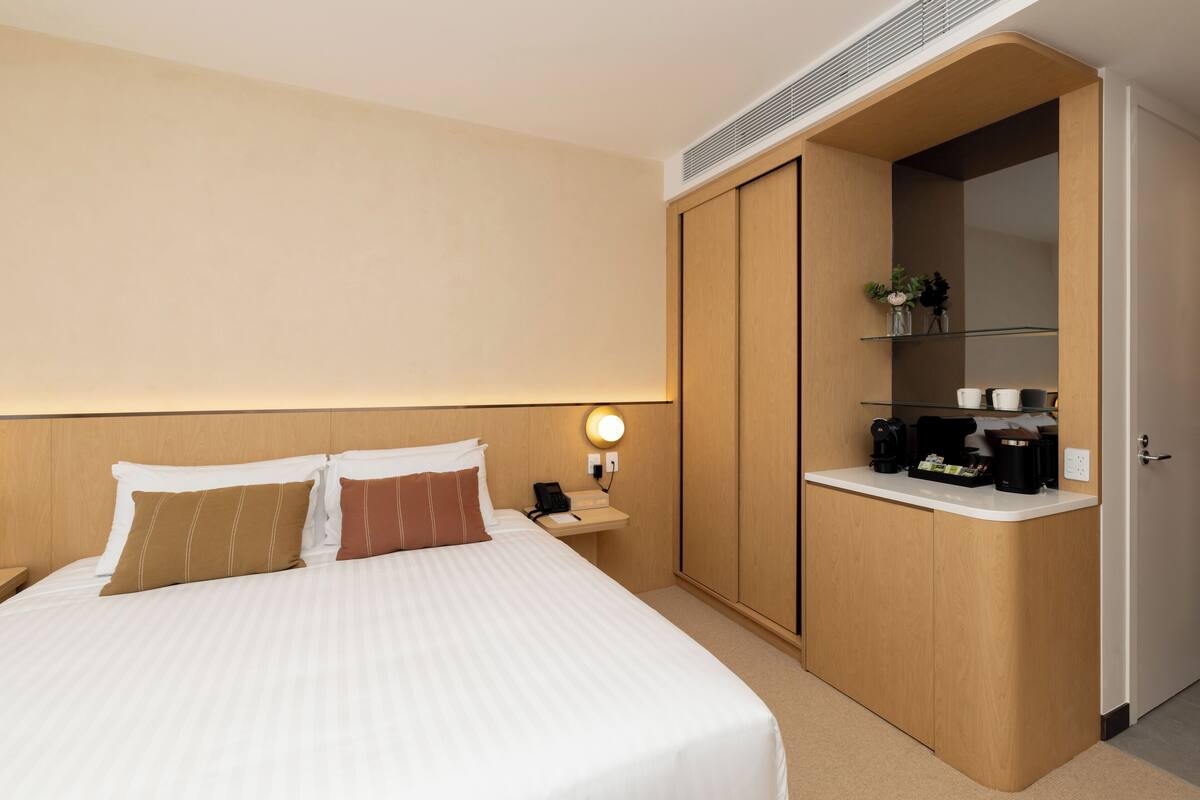 Une chambre d’hôtel comprenant un lit, une table de chevet, une lampe et un petit coin cuisine équipé d’une machine à café et d’une étagère.