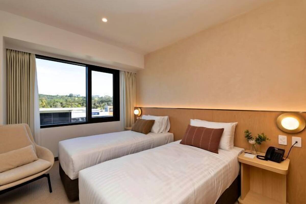 Une chambre d’hôtel avec deux lits, un canapé, une table de chevet avec un téléphone et une fenêtre avec des rideaux.