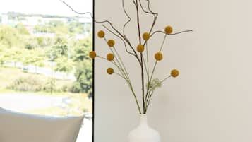 Un salon moderne avec un canapé beige, une table ronde sur laquelle repose un magazine, et un vase blanc contenant des fleurs jaunes.