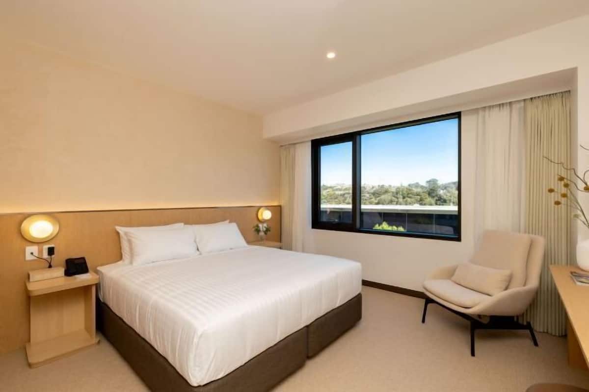Une chambre d’hôtel avec un grand lit, un bureau, une chaise, une table de chevet et une fenêtre donnant sur un beau paysage.