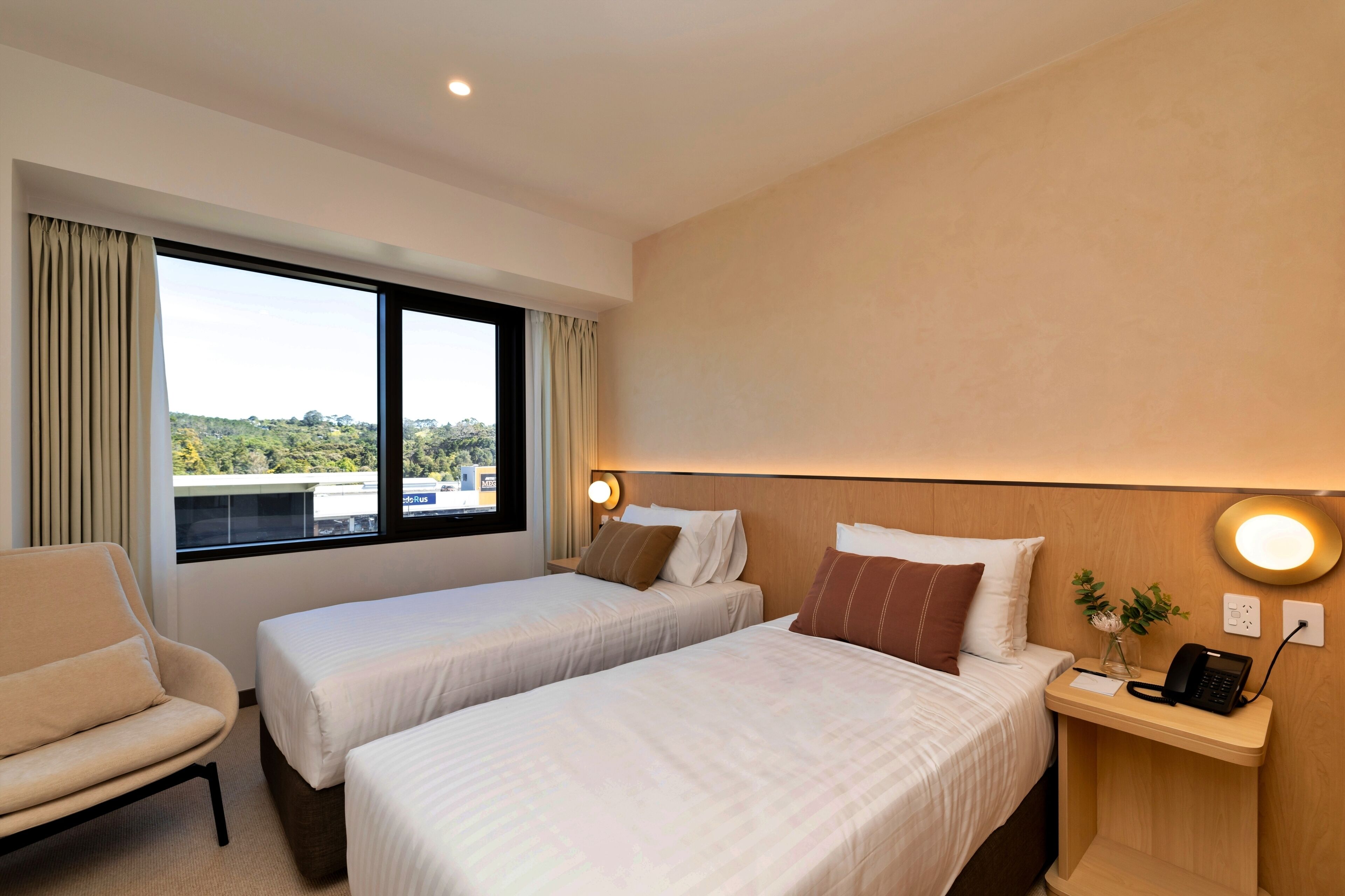 A hotel room with two beds, a chair, a bedside table with a phone, and a window with curtains.