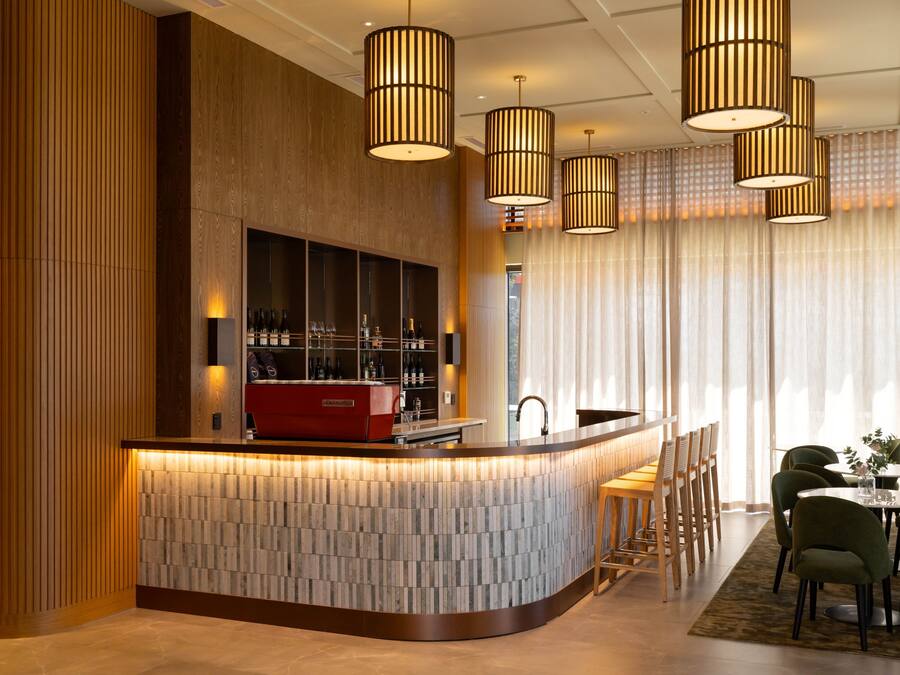 Un área de bar moderna con una barra curva, paneles de madera e iluminación colgante.
