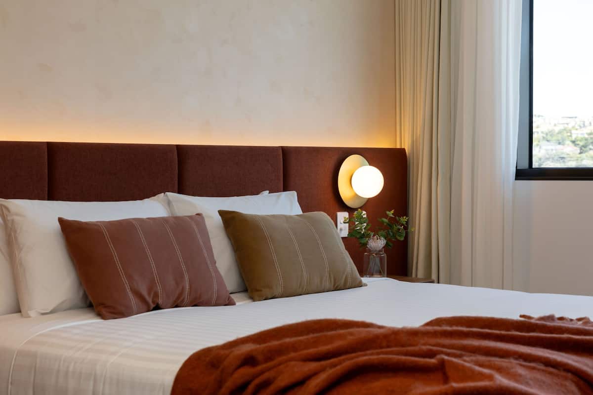 Un lit bien fait, avec une literie blanche et marron, une tête de lit marron et une lampe de chevet.