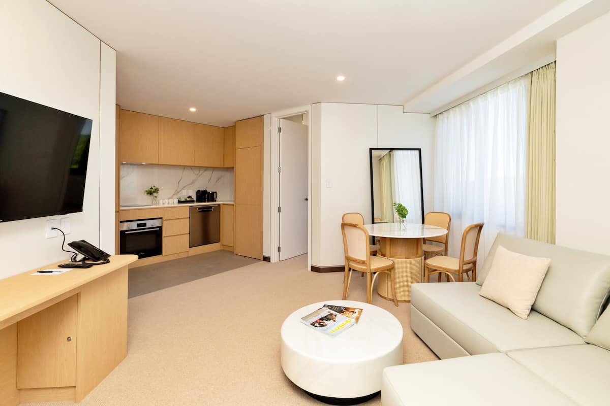 Une chambre d’hôtel moderne comprenant un coin salon, une table à manger, un canapé, une télévision et une cuisine.