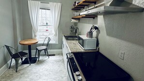A compact kitchen with a gas stove, microwave, and shelves above. There is a dining area with two chairs and a table.