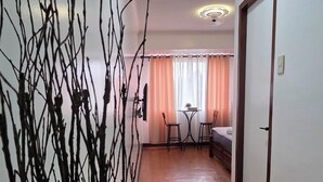 Una habitación con piso de madera, una puerta blanca, una pequeña mesa con sillas y un jarrón con ramas.