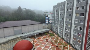 Un edificio de varios pisos con techo plano, un patio con suelo de baldosas y un objeto esférico rojo en el suelo.