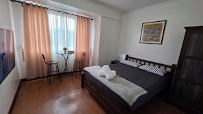 A bedroom with a bed, two chairs, a small table with a plant, and a painting on the wall.