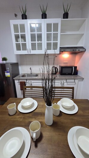 Una cocina con armarios blancos, microondas, lavabo y una mesa de comedor con platos y tazas.