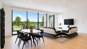 A modern living room with a round dining table, black chairs, a sofa, and a TV mounted on the wall. - The Evelyn Port Melbourne by Ready Set Stay - WIFI, linen, towels, brand new (Port Melbourne)
