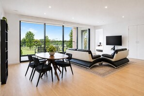 A modern living room with a round dining table, black chairs, a sofa, and a TV mounted on the wall. - The Evelyn Port Melbourne by Ready Set Stay - WIFI, linen, towels, brand new (Port Melbourne)