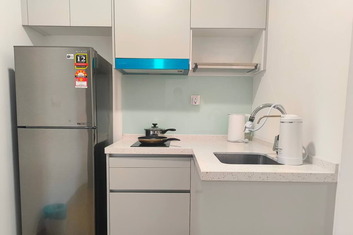 A compact kitchen with a stainless steel refrigerator, a gas stove, a sink, and a white coffee machine.