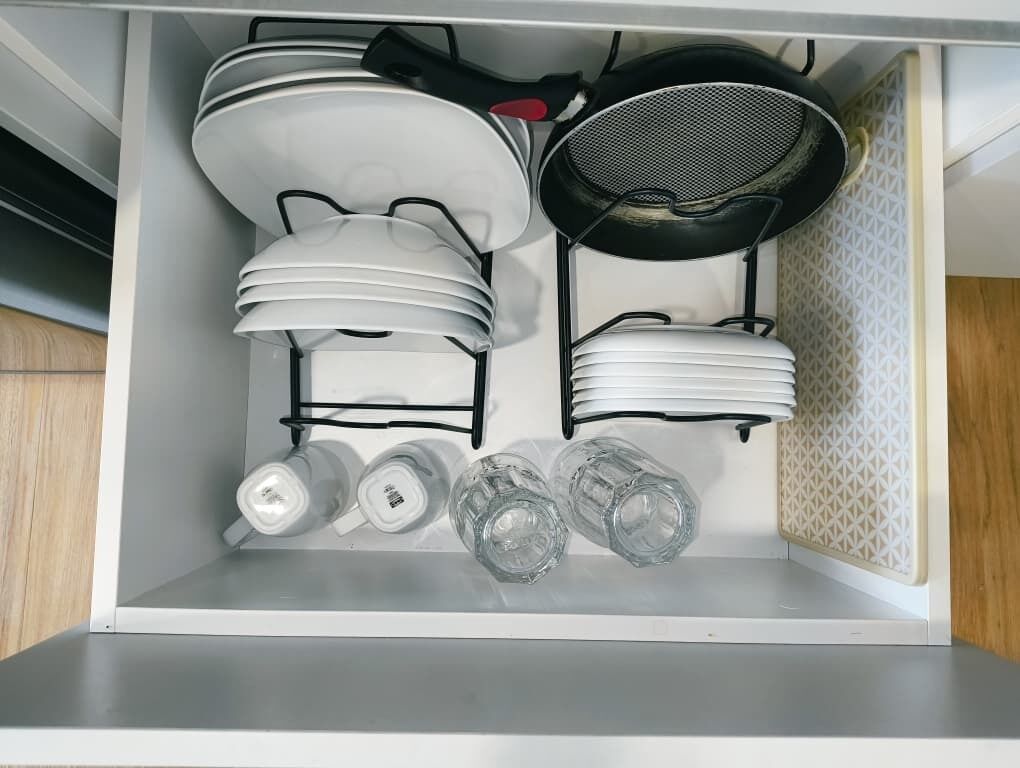 A kitchen with white cabinets, a black frying pan, stacked white plates, and three clear glasses.