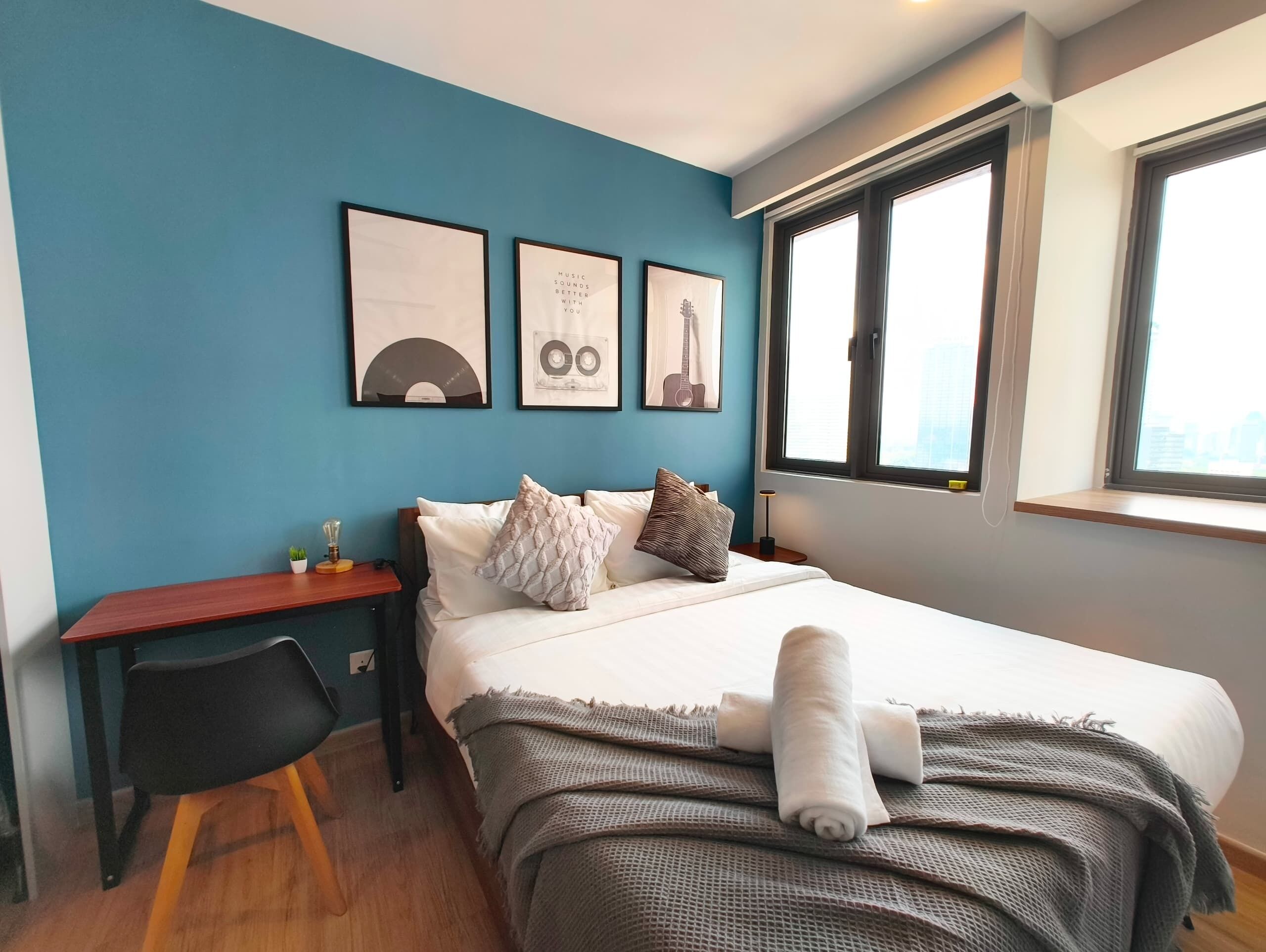 A bedroom with a bed, a desk, a chair, and a window with a city view.