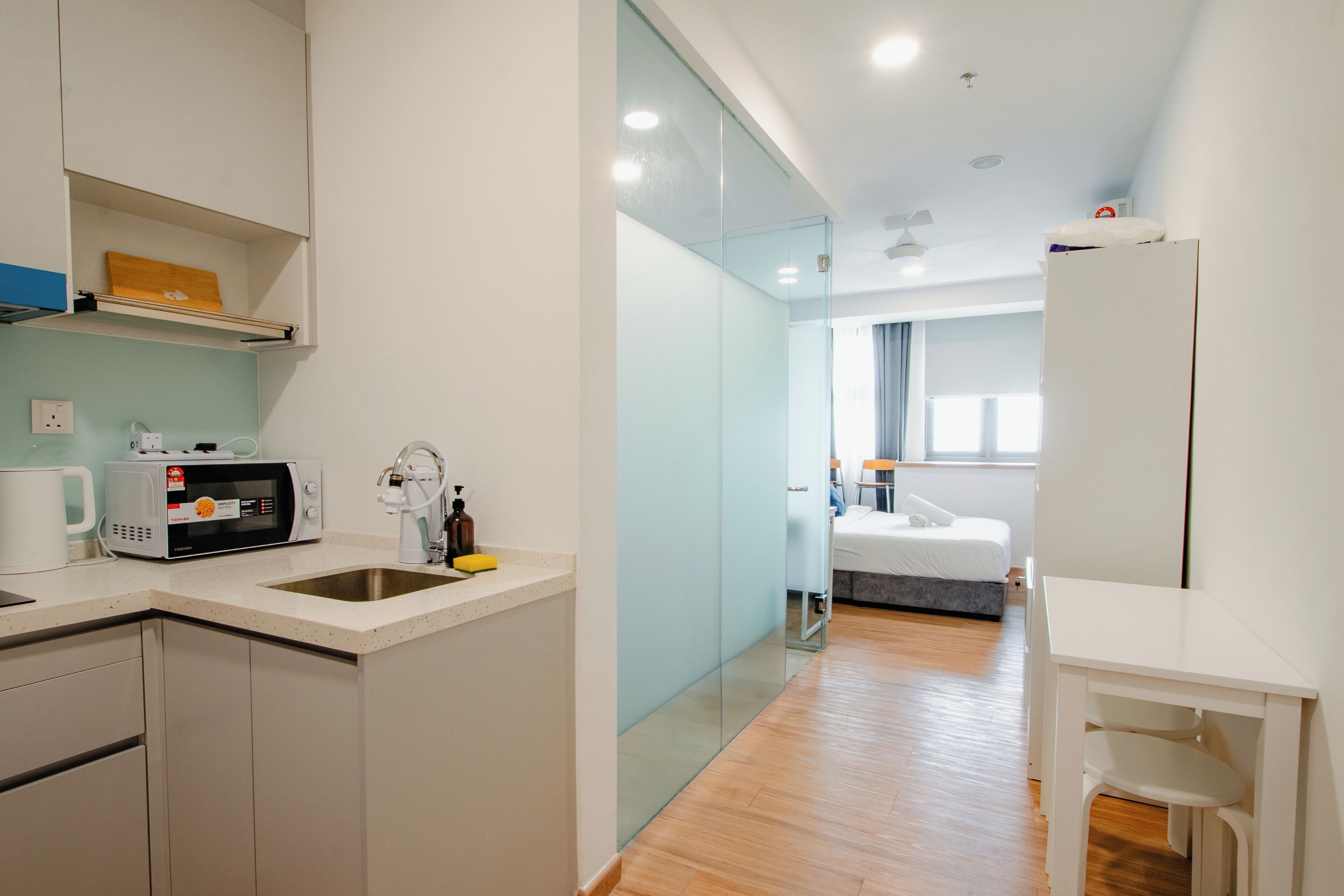 Una habitación de hotel moderna con kitchenette, una cama, una mesita y un separador de vidrio.