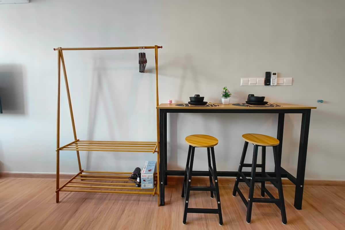 A room with a wooden floor, a desk with two stools, a hanging rack, and a wall-mounted electrical outlet.