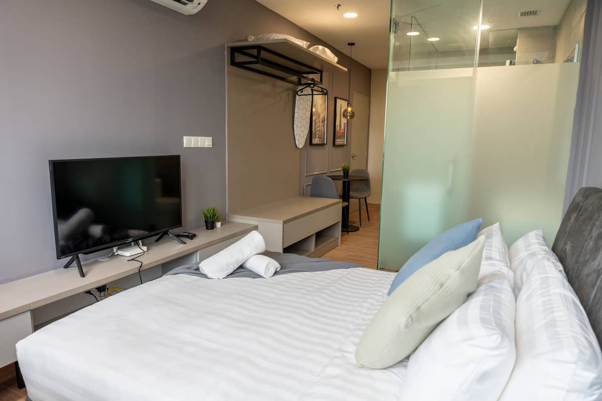 A modern hotel room with a bed, a TV, a desk, and a shower area.