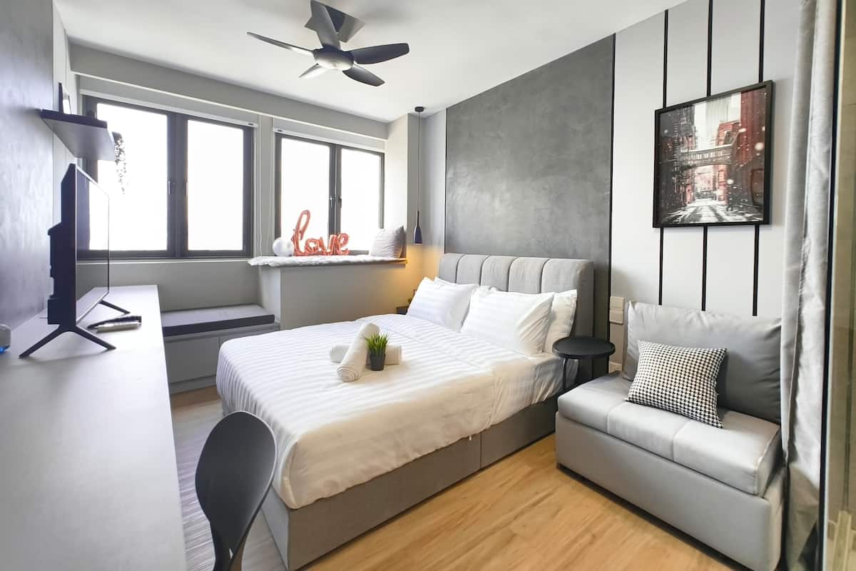 A modern bedroom with a bed, a desk, a chair, a ceiling fan, a window, and a painting on the wall.