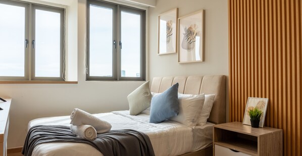 Een moderne slaapkamer met een groot bed, een nachtkastje en een raam met jaloezieën.