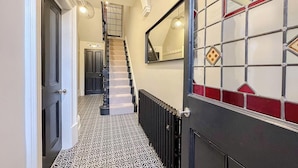 Un pasillo con piso estampado, una escalera y una puerta de vidrio decorativa.