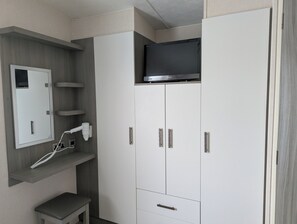 Une pièce équipée d’un téléviseur encastré, d’une armoire blanche, d’un banc et d’une prise électrique murale.