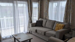 Un salon avec un canapé gris, une table basse en bois et des rideaux en voile.