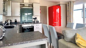 Une cuisine compacte équipée d’une cuisinière, d’un évier et de placards, un coin repas avec une table et des chaises, et un appareil électroménager rouge en arrière-plan.