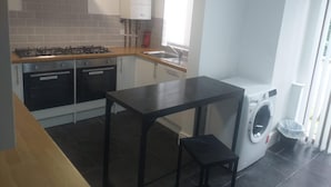 A compact kitchen with a gas stove, two ovens, a built-in washing machine, and a small table.