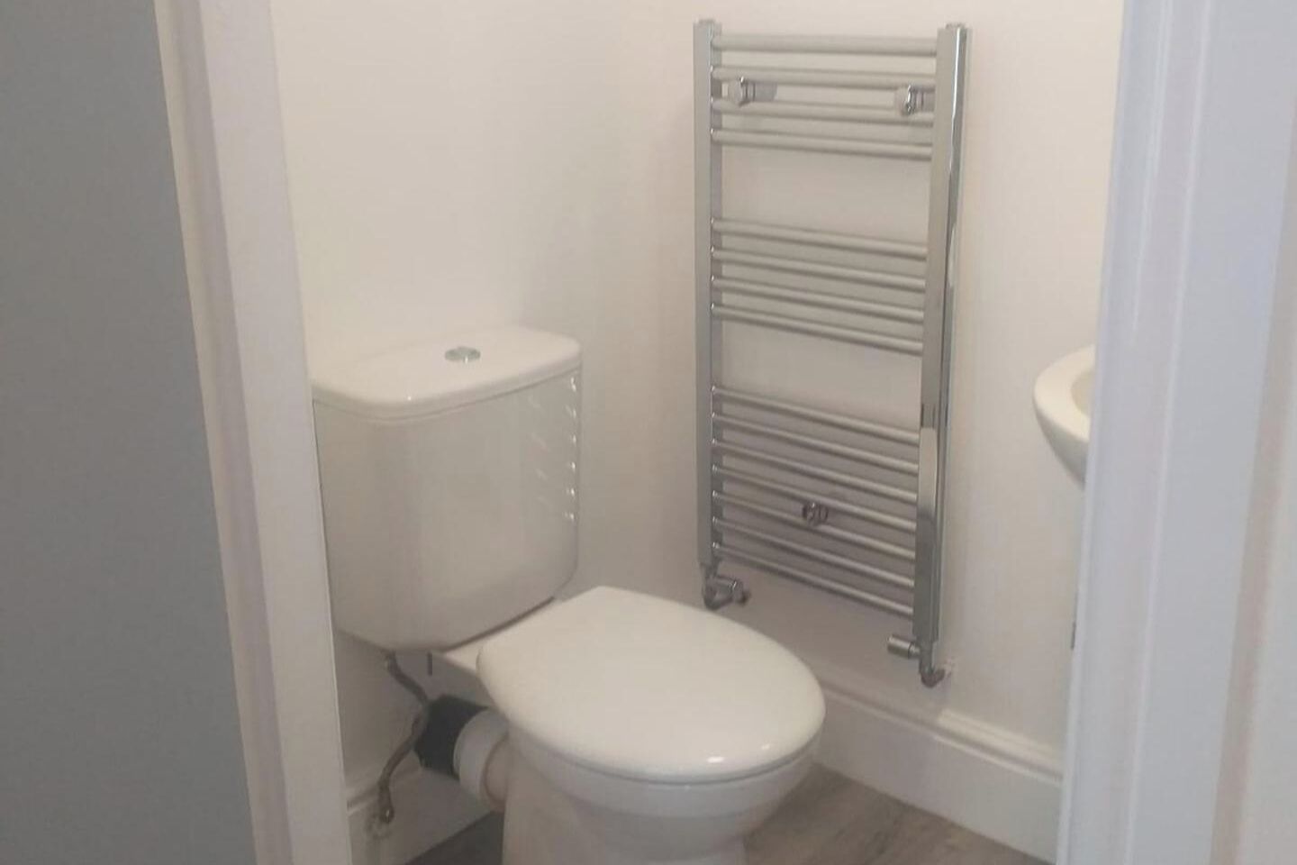 Une petite salle de bain blanche, avec des toilettes, un porte-serviettes chromé et un lavabo blanc.