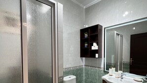 Une salle de bain moderne avec une douche à parois de verre, des toilettes, un lavabo avec un miroir et un meuble contenant des articles de toilette.