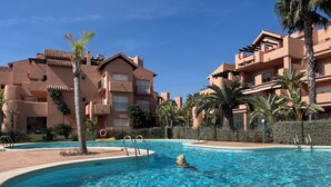 A swimming pool surrounded by multi-story buildings with balconies and palm trees. - Mediterranean View, in Mar Menor Golf Resort (Torre Pacheco)