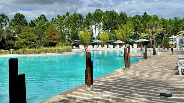 Un espace aménagé au bord de la piscine, avec une piscine à l’eau d’un bleu limpide, des chaises longues et une allée dallée.