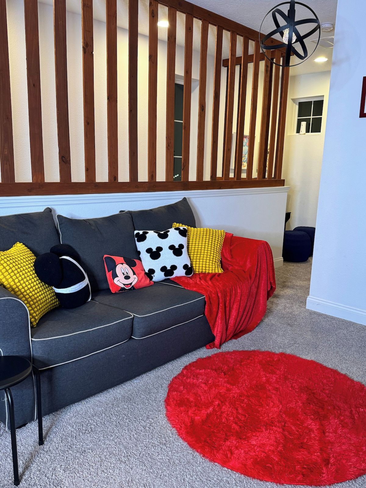A modern living room with a grey sofa, red throw blanket, and various colorful pillows.