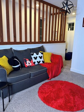Una sala moderna con un sofá gris, una manta roja y varios cojines coloridos.