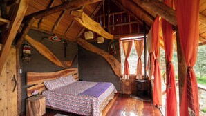 A rustic wooden room with a bed, a small table, and a window with curtains. - Amanecer Andino (Rest cabin in the mountain) (Puyo)