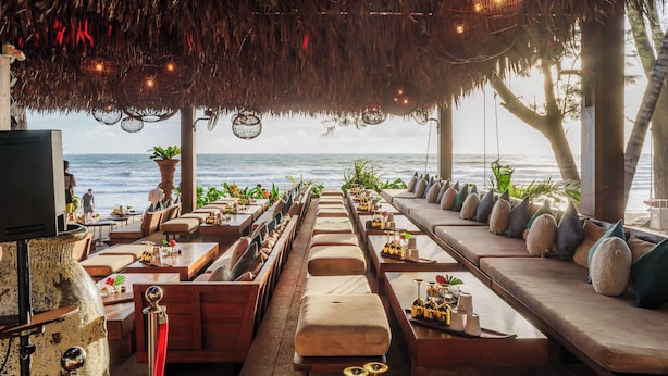 A beachside restaurant with outdoor seating, a thatched roof, and ocean views. - Cafe del Mar Hotel (Kamala)