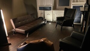 Een woonkamer met een bruine bank, een zwarte fauteuil en een houten vloer.