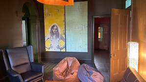 Een kamer met een groot abstract schilderij, een lederen fauteuil, een kruikzak en een deur naar een andere kamer.