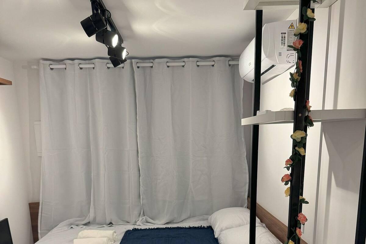 Habitación compacta con cama, escritorio, lámpara en el techo y aire acondicionado de pared.