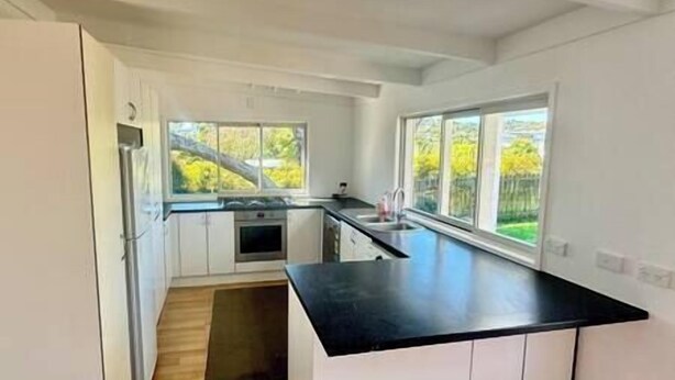 A modern kitchen with white cabinets, a black countertop, and large windows offering a view of greenery outside. - Miami one one - Superior King Studio - Walk to Beach, Village and 2 Vineyards (Waiheke Island)