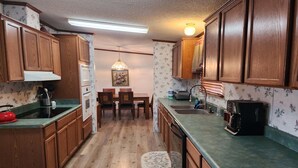 A kitchen with wooden cabinets, a dining table, and a coffee maker. - Rancho Mula Oso PLUS Bunkhouse: Unparalleled Outdoor Space (Terlingua)