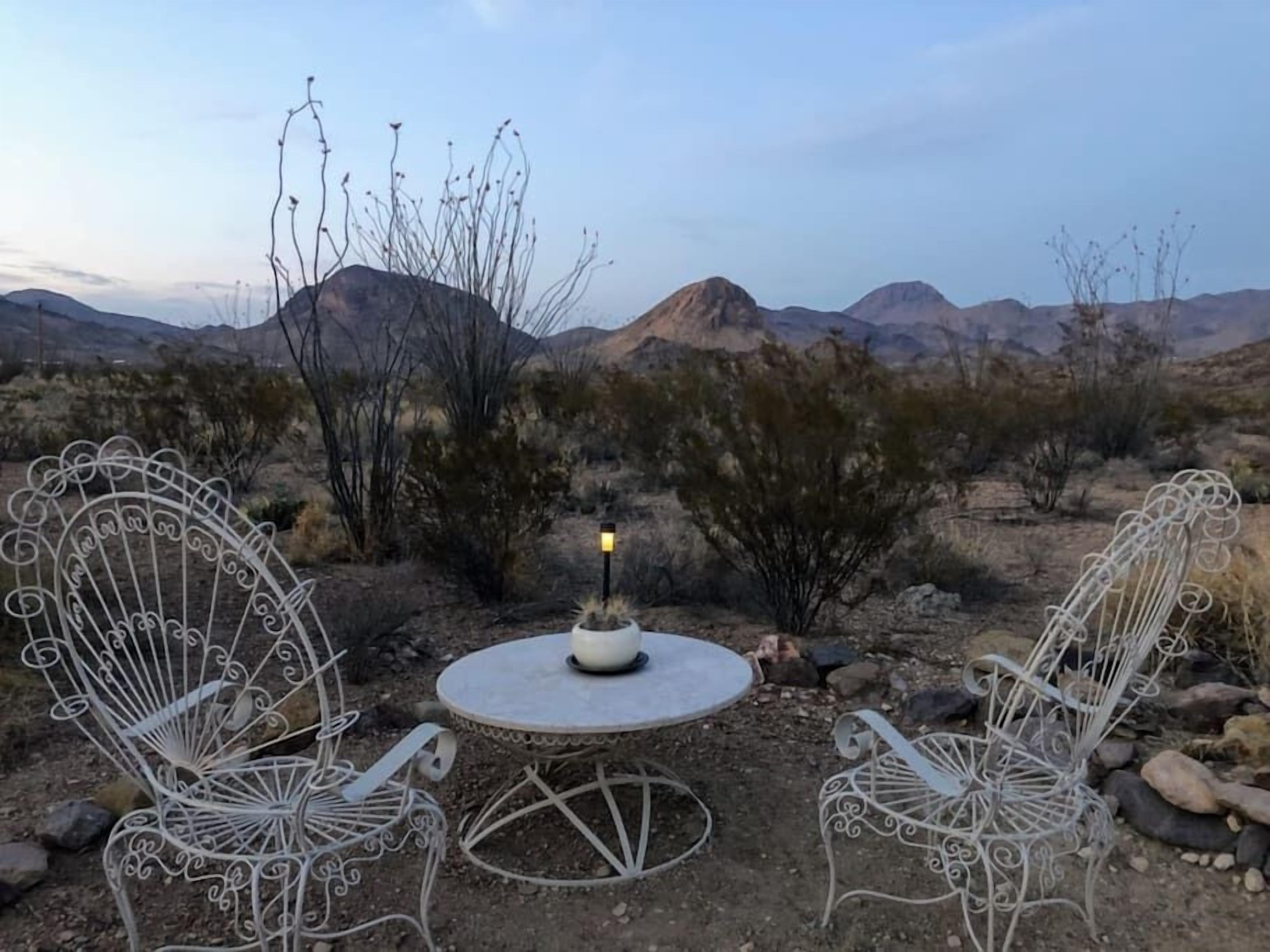 Un paysage désertique avec une table et des chaises en métal, une plante en pot et une petite lampe.