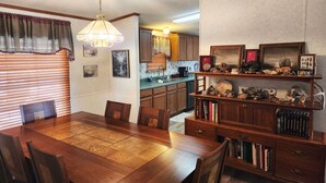 A dining area with a wooden table and chairs, a chandelier, and a kitchen with wooden cabinets and a countertop. - Rancho Mula Oso PLUS Bunkhouse: Unparalleled Outdoor Space (Terlingua)